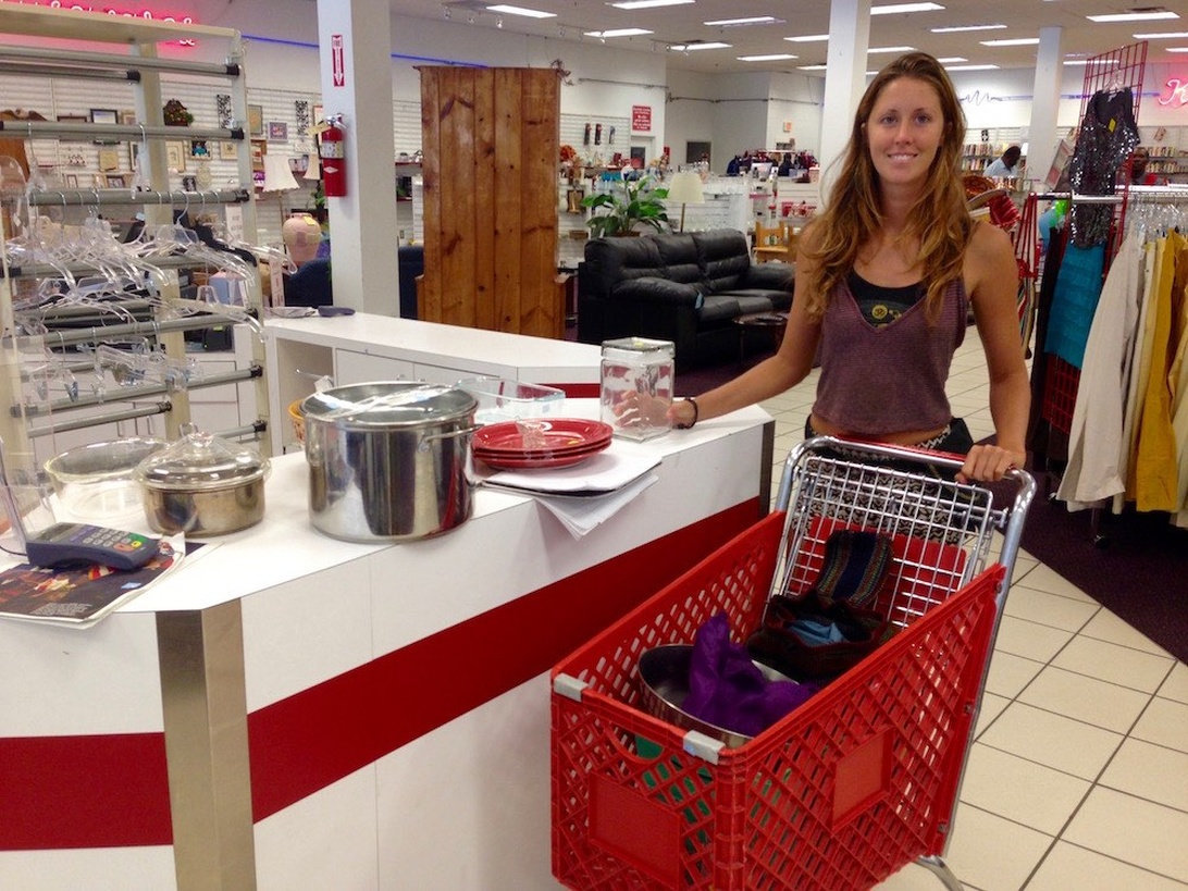 A retail store scene showing a shopper with a shopping cart containing what appears to be stainless steel pots or cookware on a checkout counter. While cookware is visible, the image is primarily about the shopping experience rather than highlighting features of healthy cooking equipment.