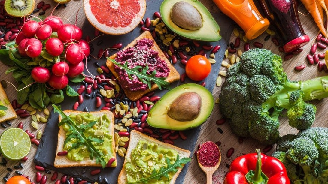 En färgstark uppläggning av vegansk mat, inklusive avokadotoast och ett urval av färska frukter och grönsaker.