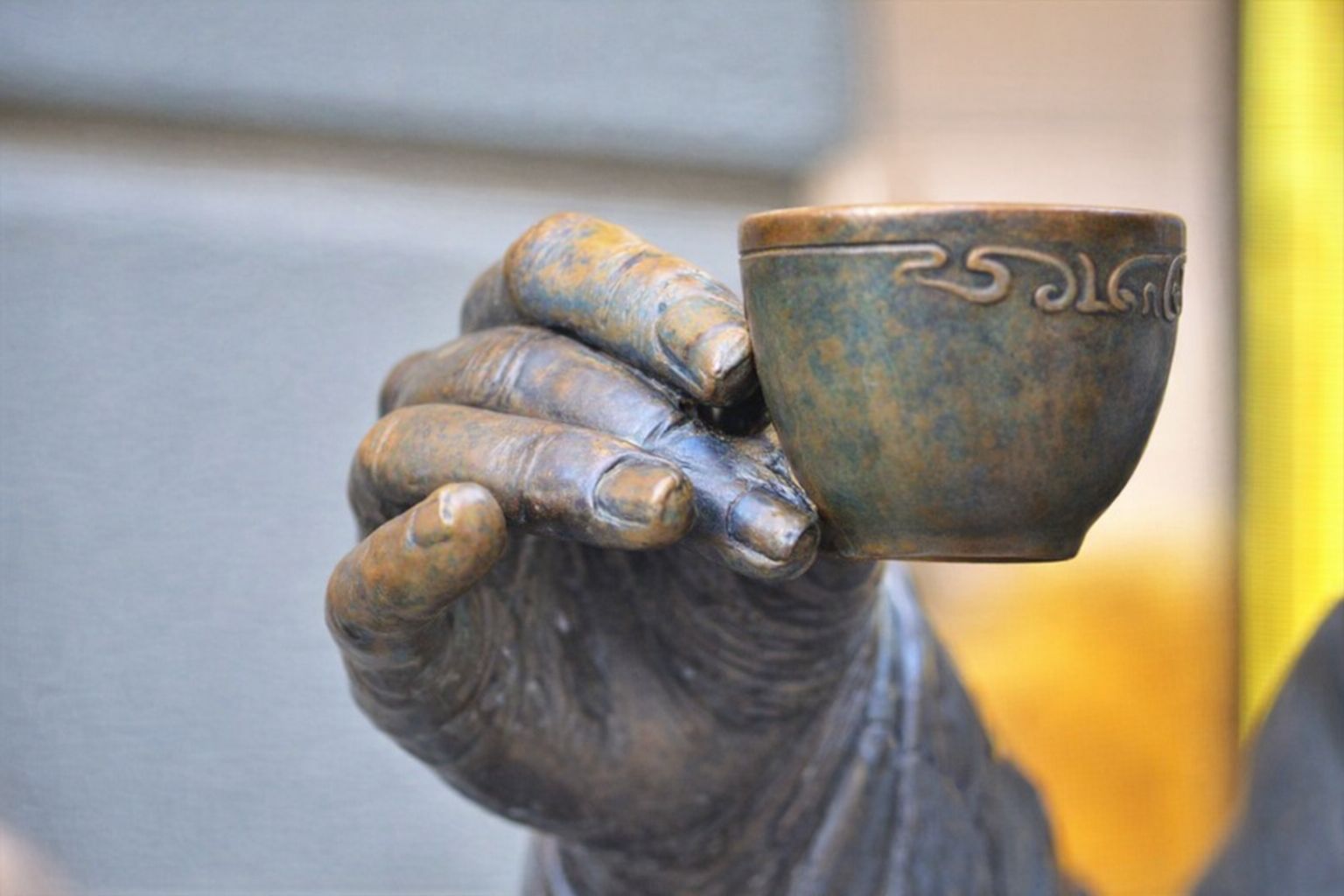 Närbild på en statyhand i brons som håller en liten dekorerad kopp.