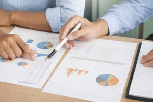 Händer som analyserar ekonomiska grafer och tabeller vid ett skrivbord.