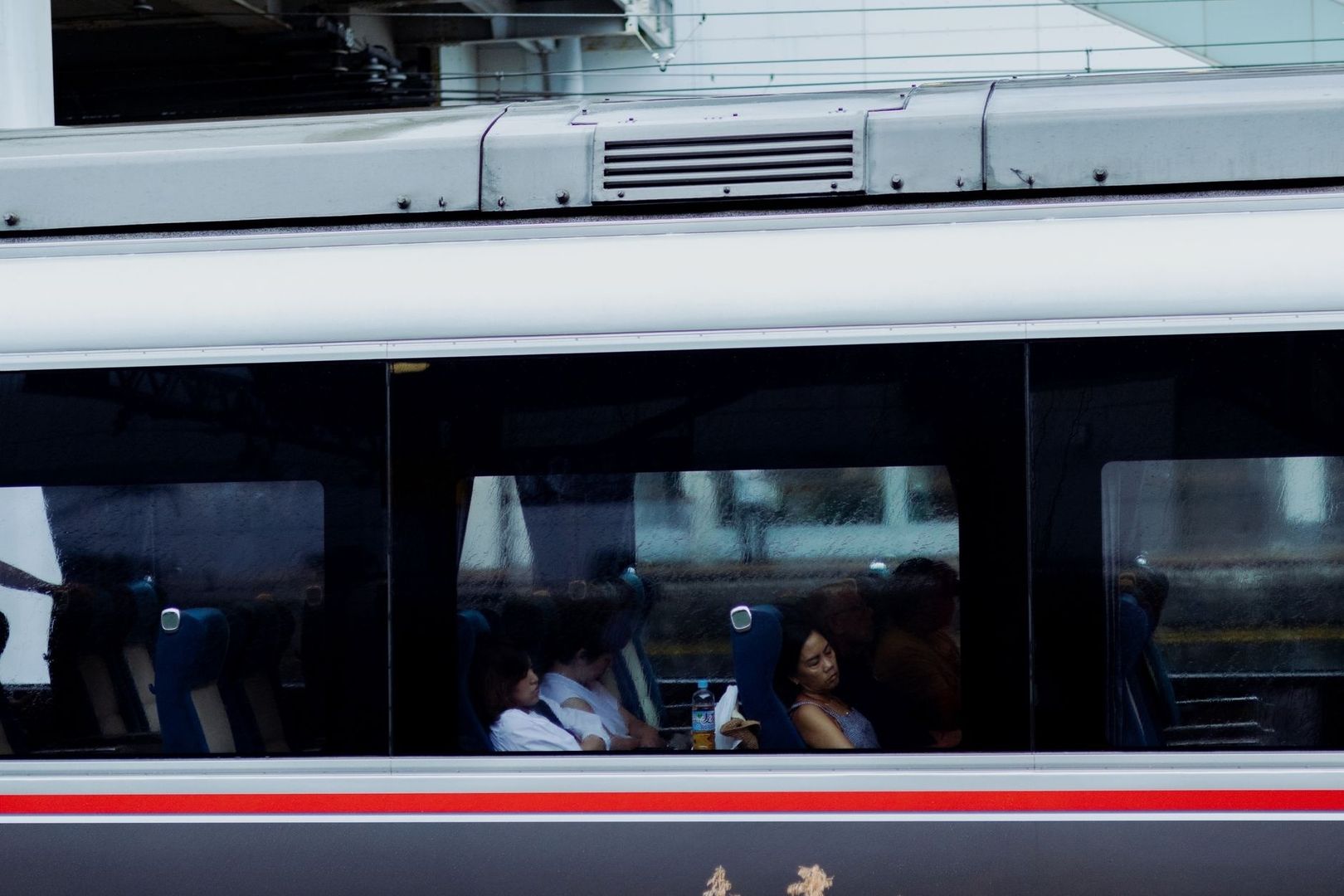 Passagerare sitter tysta i en tågvagn, sedda genom fönstret